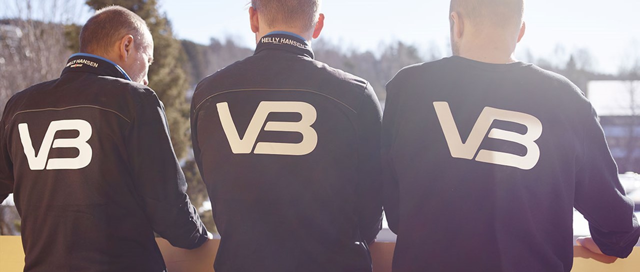 Tre VB Rørleggere med ryggen til kamera og VB logo på arbeidsklærne